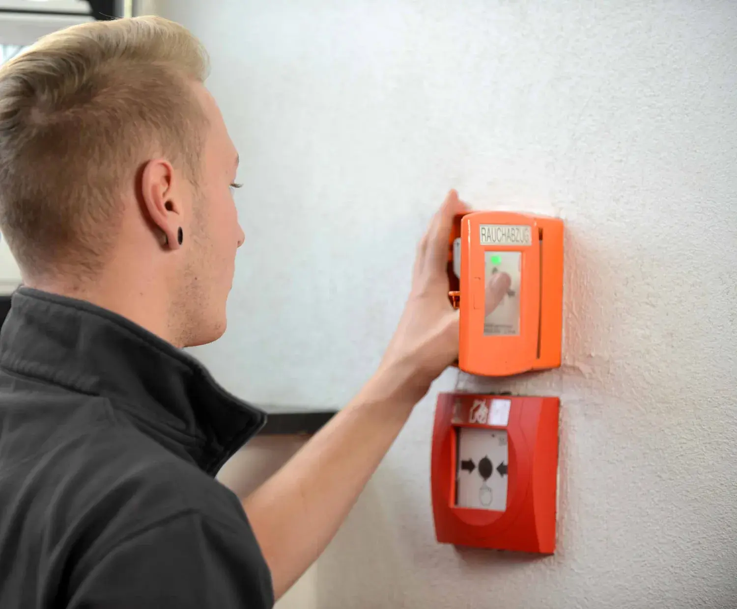 Brandschutztechniker drückt auf den Knopf eines Handtasters einer RWA-Anlage