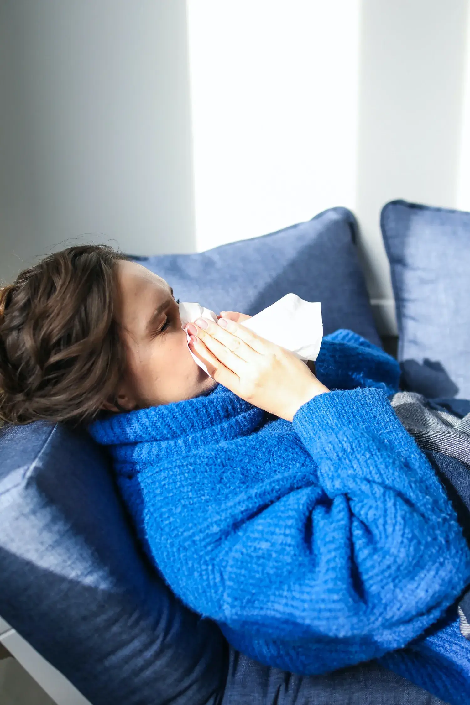 Žena s chřipkou kýchající do papírového kapesníku