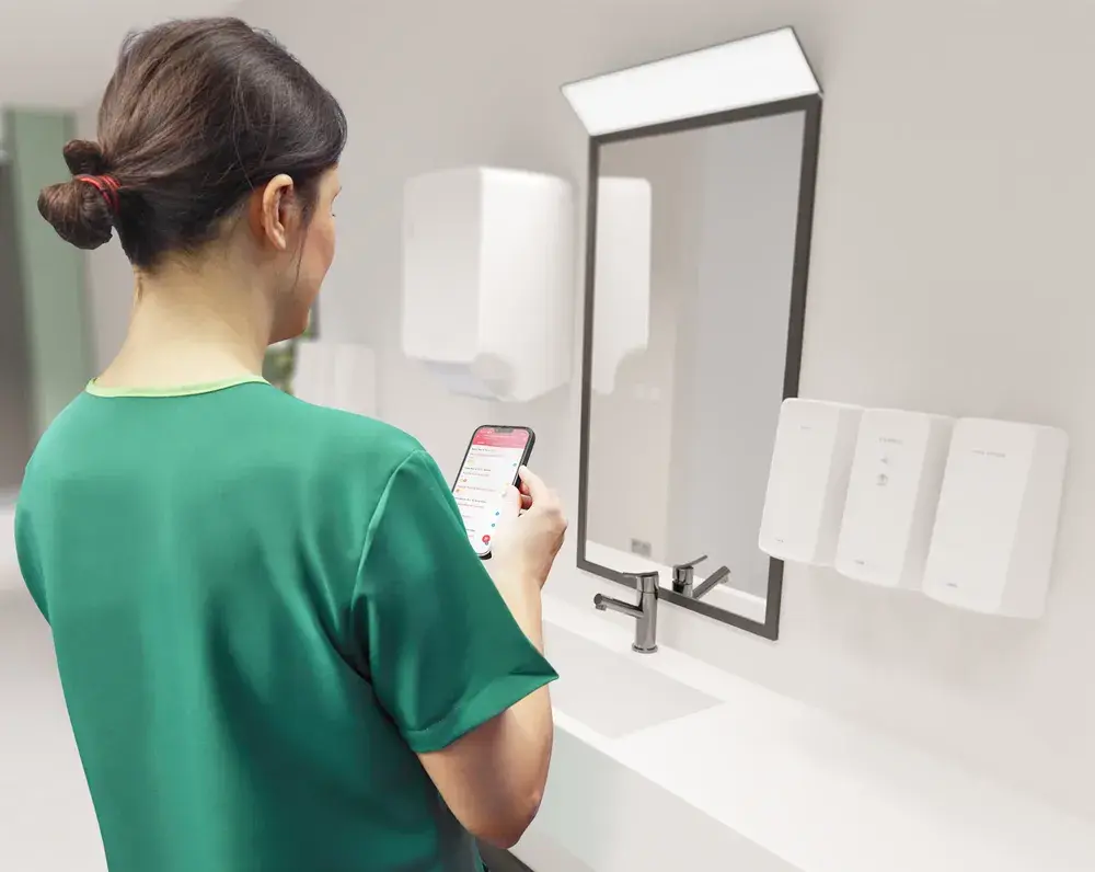 Cleaner uses the CWS smartMate app in a washroom with dispensers mounted on the wall