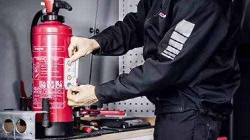 CWS Servicetechniker Brandschutz klebt Instandhaltungsetikette auf Feuerlöscher