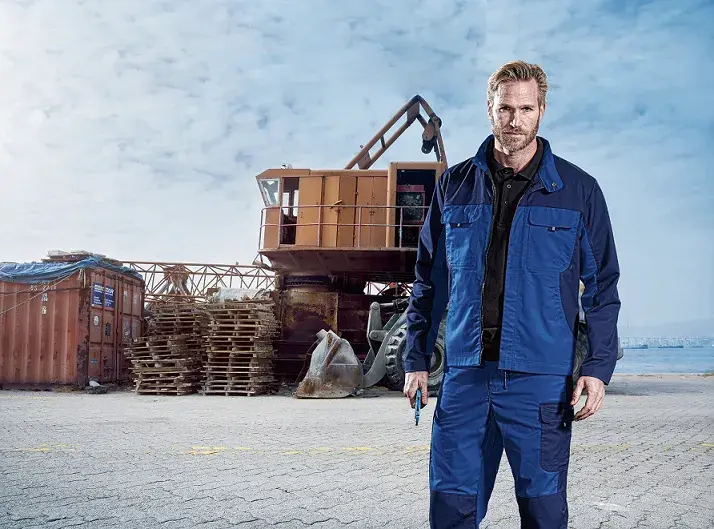 CI Workwear: Mann in Compact Line Jacke und Hose (blau/dunkelblau) auf einer Baustelle