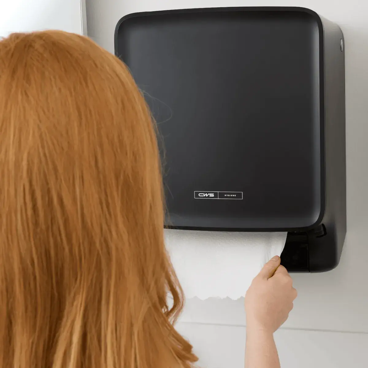 Woman uses a CWS PureLine EcoBlack Paperroll dispenser