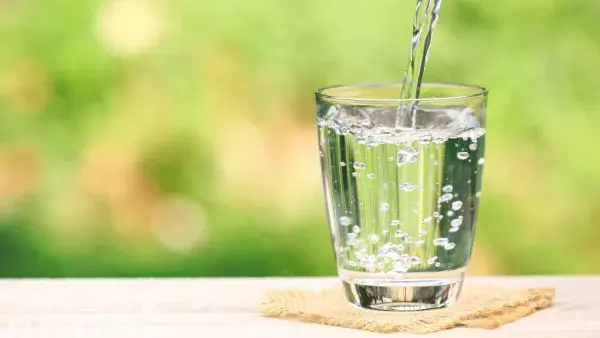 Wasserglas, das mit sprudelndem Wasser gefüllt wird mit grünem, verschwommenem Hintergrund